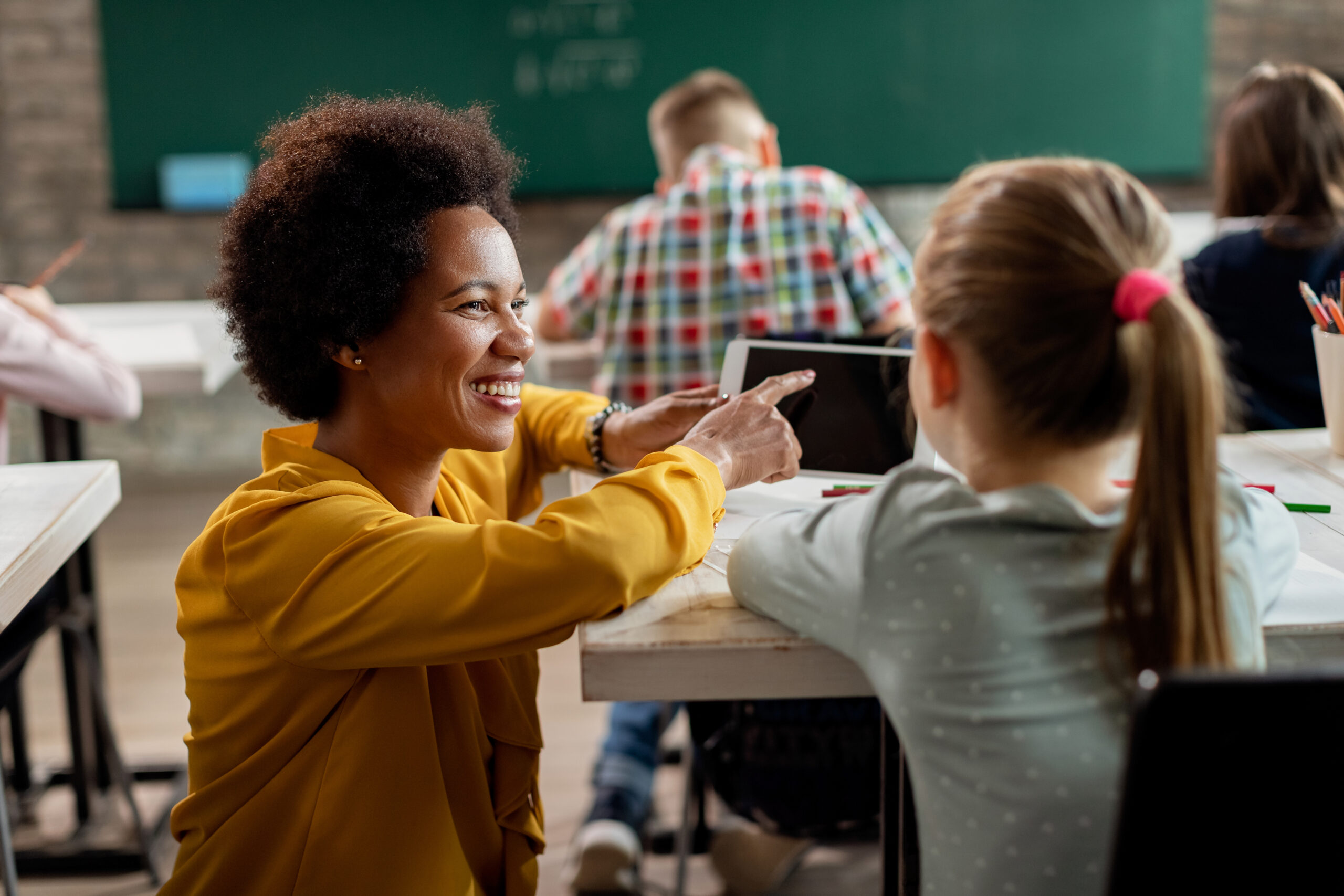 Happy African American teacher and elementary student using touchpad during a class in the classroom.